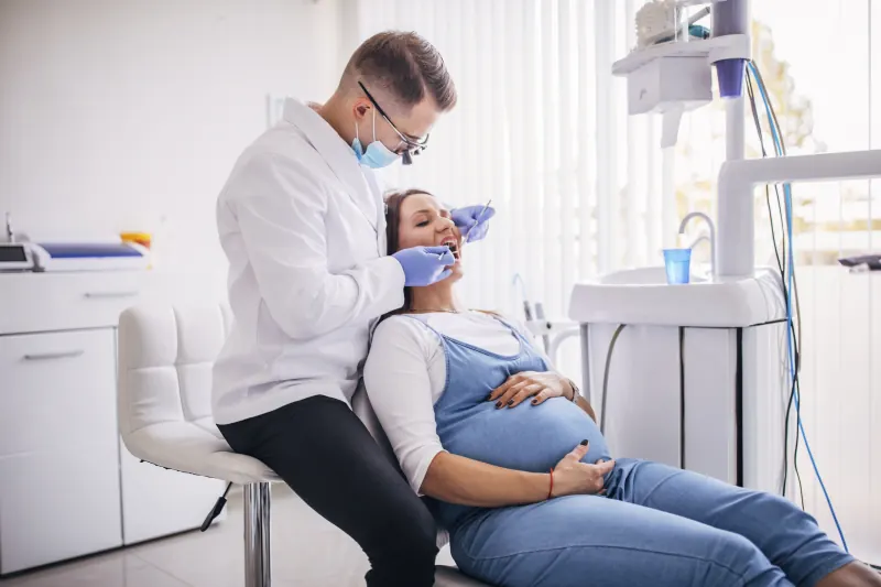 Gestante sentada na cadeira odontológica sendo atendida pelo dentista