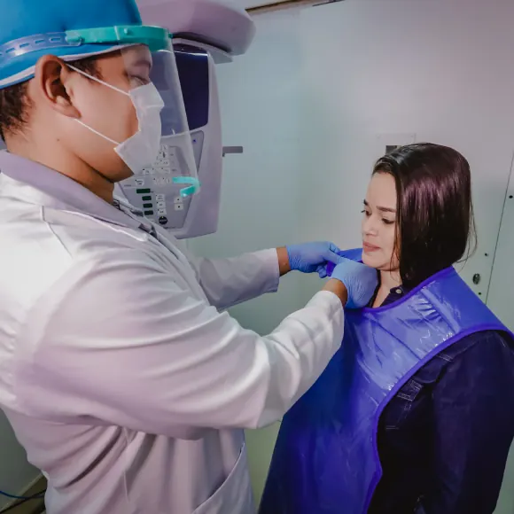 Paciente com avental de proteção posicionada no aparelho de raio-X odontológico