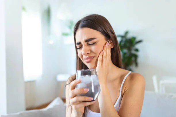 Mulher com a mão no rosto, com expressão de dor ao beber um copo de água com gelo