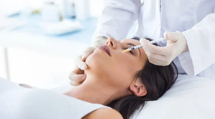 Mulher deitada recebendo aplicação de botox perto dos olhos, feita por profissional de jaleco