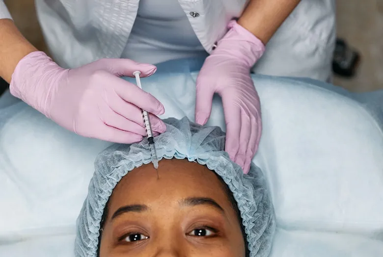 Profissional de luvas aplicando toxina botulínica na testa de uma paciente
