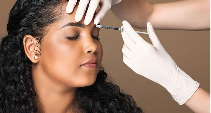 Profissional de luvas aplicando botox entre as sobrancelhas de uma paciente de olhos fechados