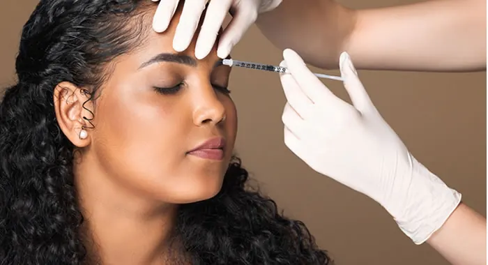 Mulher jovem de olhos fechados recebendo aplicação de toxina botulínica na testa