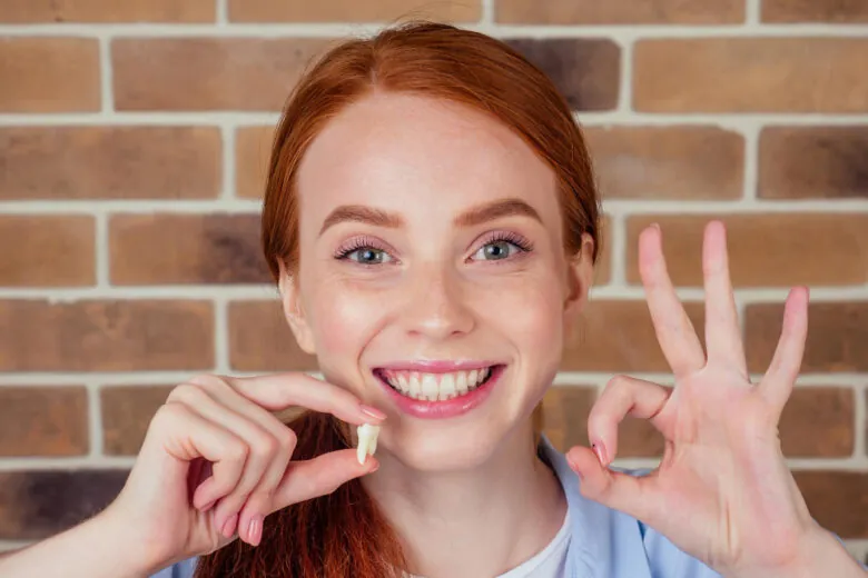 Mulher sorrindo e segurando um dente siso extraído