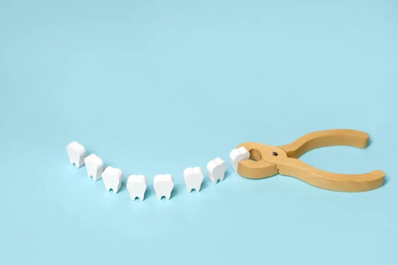 Fileira de dentes de brinquedo e um alicate de madeira sobre fundo azul