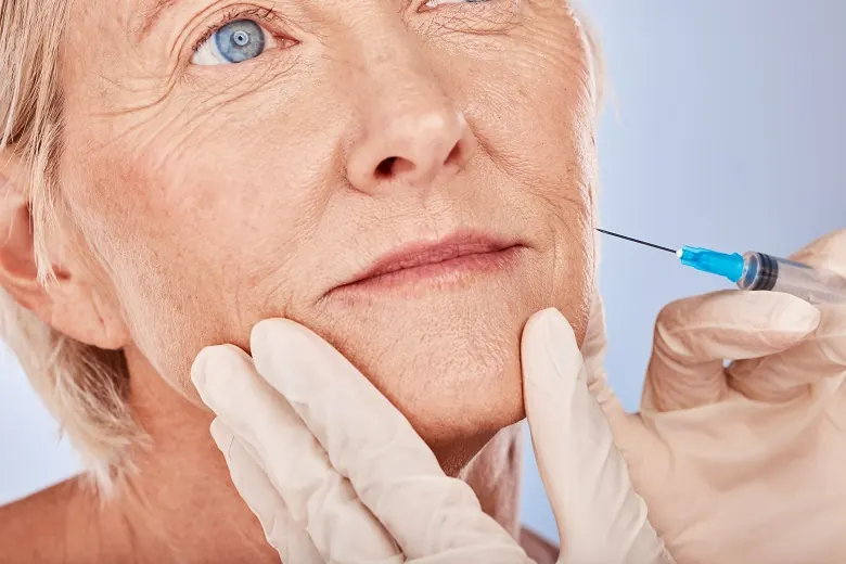 Profissional de luvas aplicando toxina botulínica no rosto de uma mulher madura