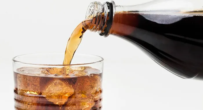 Refrigerante de cola sendo servido em um copo com gelo