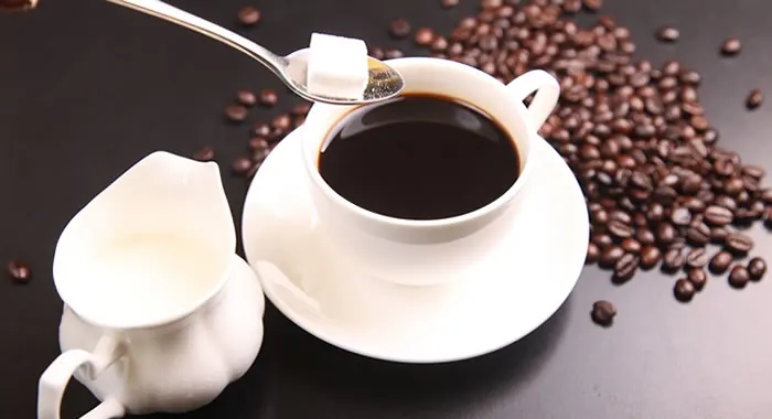 Xícara de café com leite ao lado de grãos de café