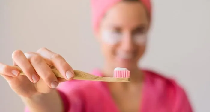 Mulher estendendo uma escova de dente de bambu com creme dental