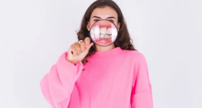 Mulher segurando uma lupa diante da boca, mostrando os dentes e a gengiva