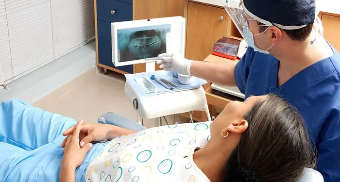Dentista mostrando uma radiografia panorâmica no monitor para a paciente deitada na cadeira