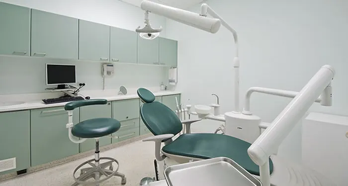 Consultório odontológico vazio e organizado, com cadeira odontológica, refletor e bancadas