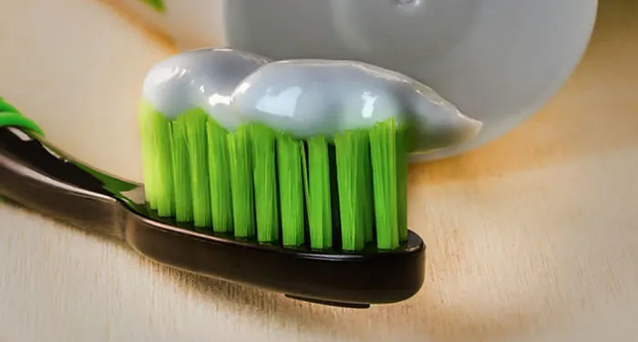 Escova de dente com cerdas verdes e creme dental sobre a cabeça