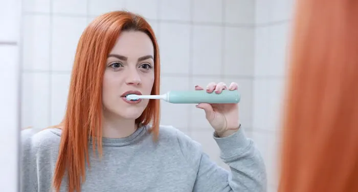 Mulher escovando os dentes com escova elétrica no banheiro