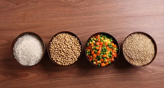 Quatro tigelas com grãos, sementes e legumes picados sobre mesa de madeira