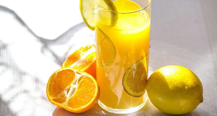 Copo de suco de laranja com rodelas de limão, ao lado de laranja e limão cortados
