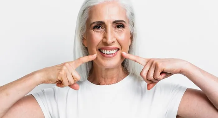 Senhora sorrindo e apontando para os dentes