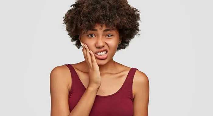 Mulher com a mão no rosto, sentindo dor de dente