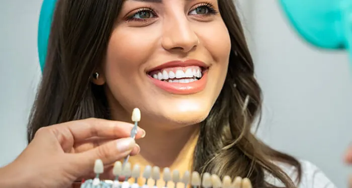 Mulher sorrindo enquanto um profissional mostra uma escala de cores de dentes