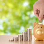 Fundo verde desfocado, cofre em formato de porco e algumas moedas à frente